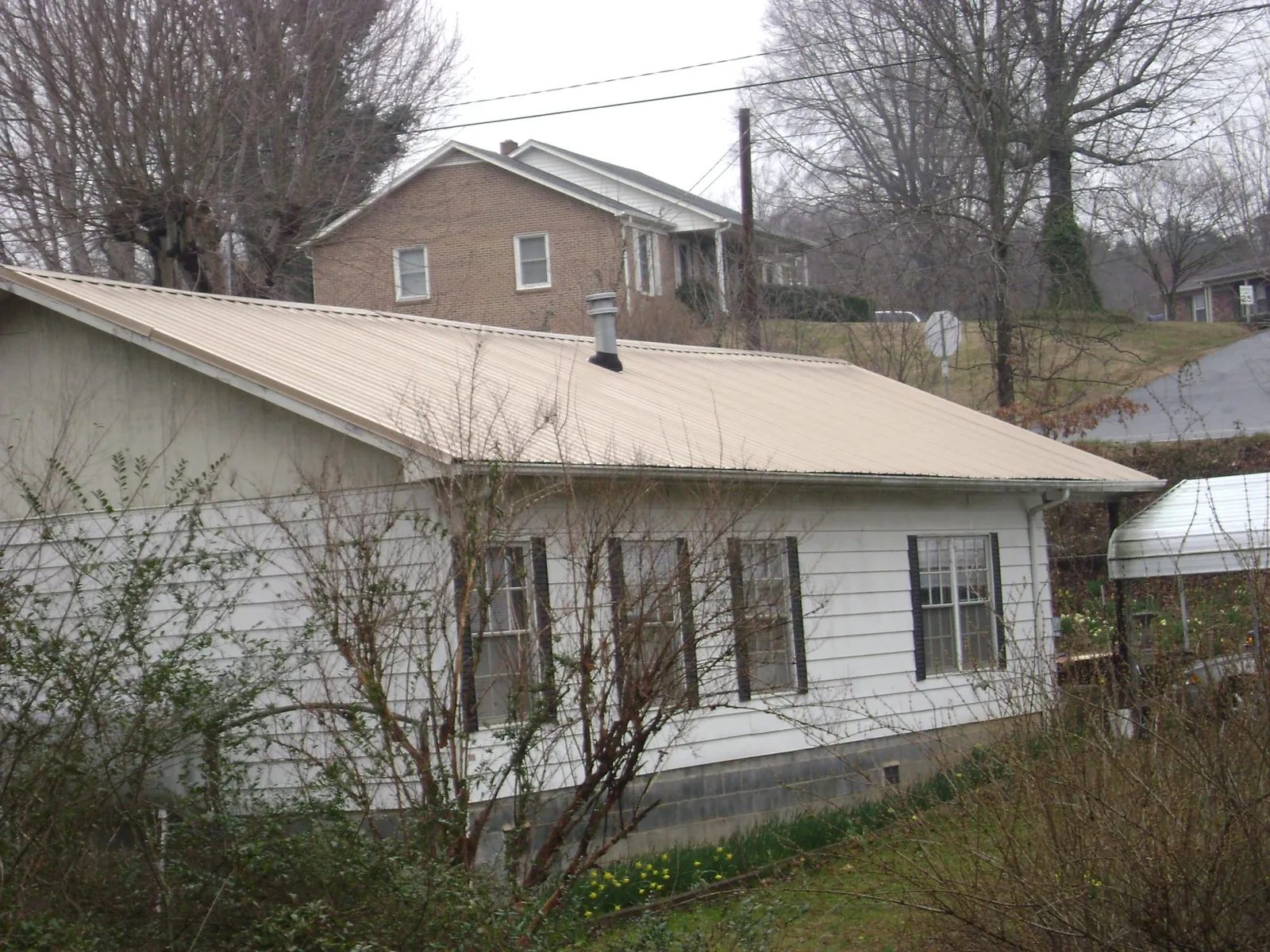 Tan metal roof on a white sided house set into a hillside — Commercial Roofing by Roofing Brothers in Hudson